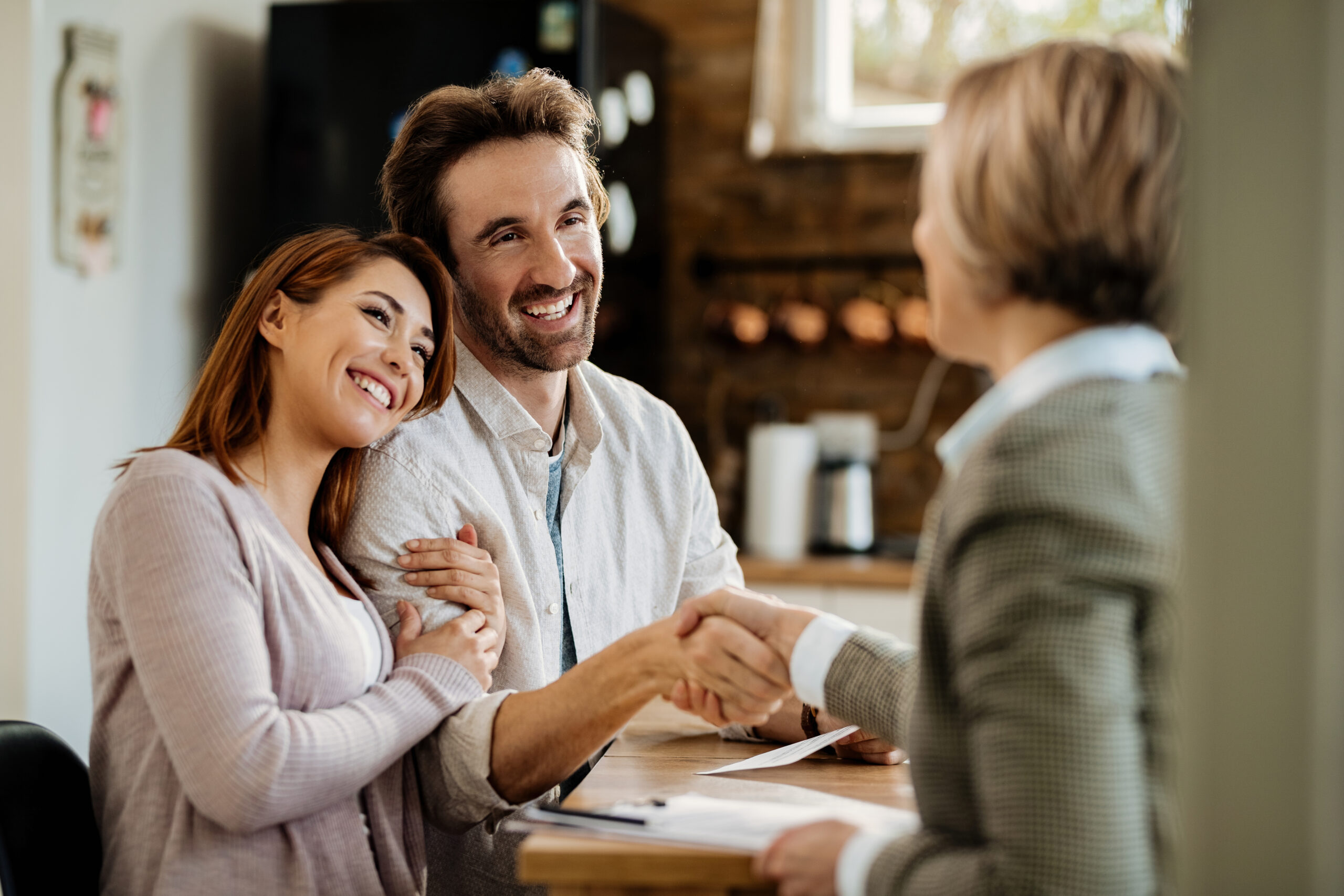 Young happy couple came to an agreement with their mortgage broker. Focus is on man shaking hands with the agent.