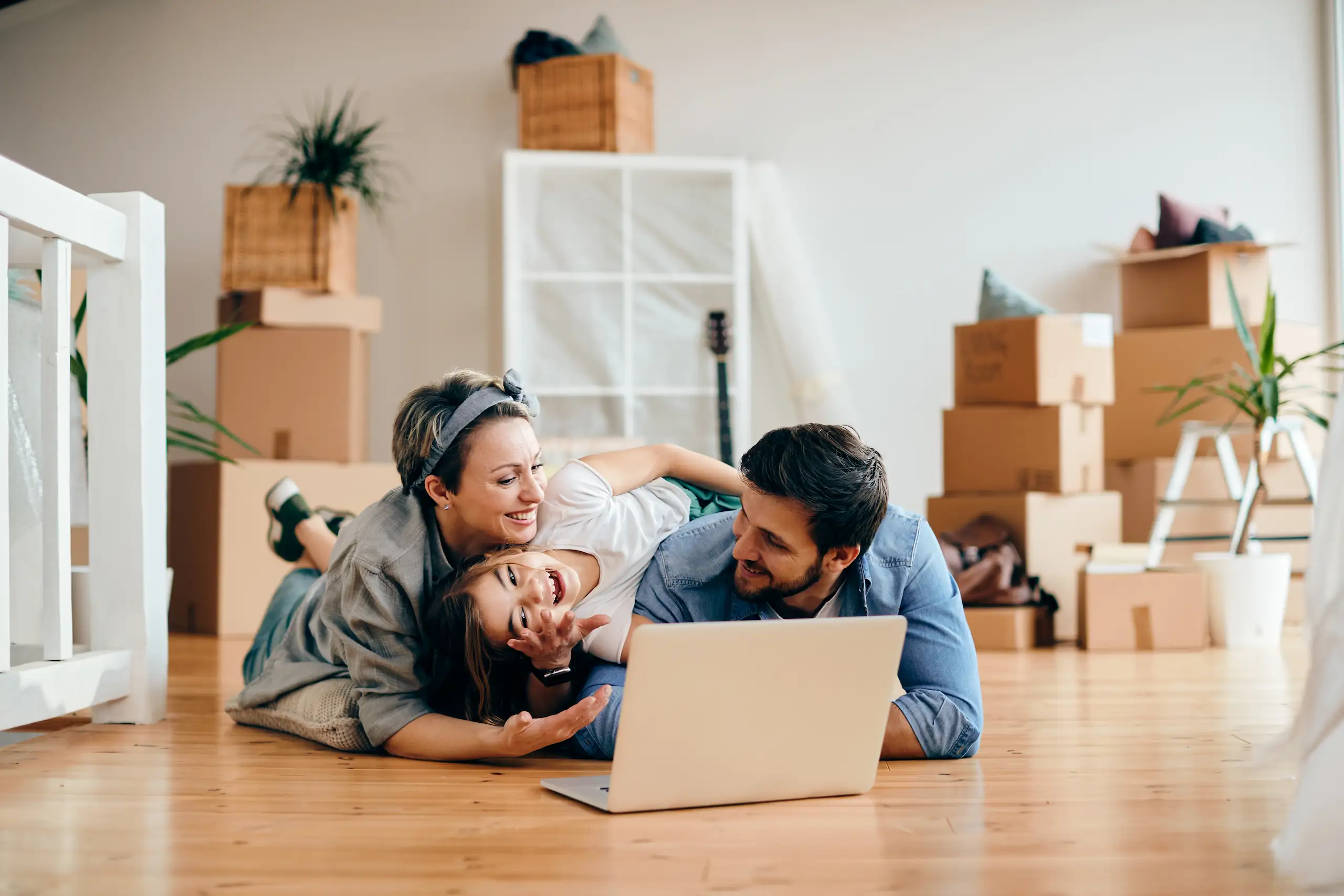 Happy family using a laptop on the floor in their new house, showcasing the financial peace of mind from having Mortgage Protection Insurance.