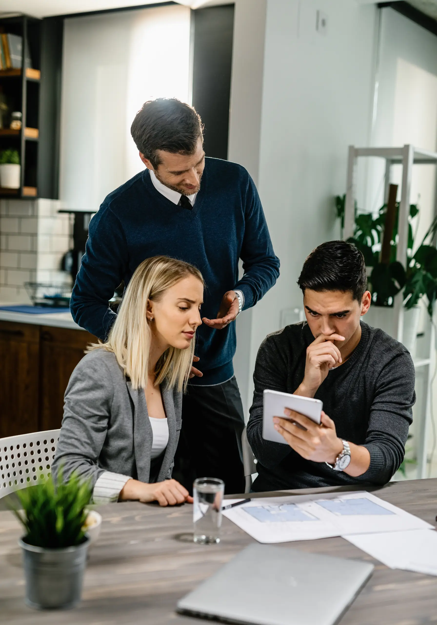 Young couple looking uncertain while using a digital tablet during a home meeting with their expert Remortgage Advisors.